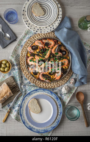 Paella on the metal plate on the beautiful napkin with tableware and bread vertical Stock Photo