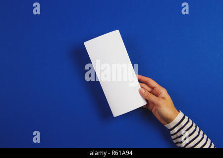 Woman hands holding blank white flyer brochure booklet. Mockup sheet template advertising booklet on blue background Stock Photo