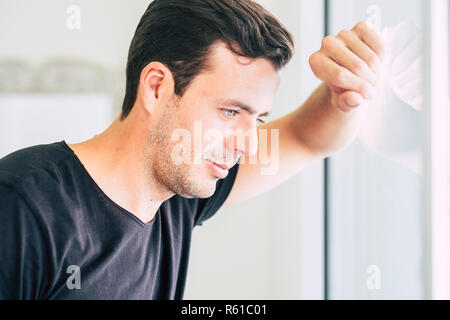 handsome beautiful blue eyes caucasian black hair model man look outside the window lost in his thoughts - people alone at home thinking to the future Stock Photo
