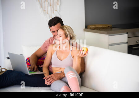 Nice happy young millennial couple in love at home sit down close on the couch - the man work at laptop digital nomad free the woman have sportwear fi Stock Photo