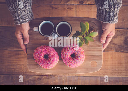 Top view of woman's hands taking two coffee and pink donuts for breakfast - fat weight loss diet junk food concept but tasty and nice to eat - sweet c Stock Photo