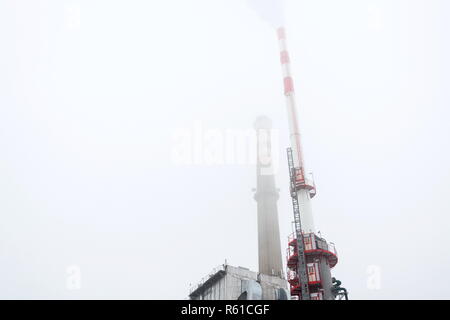 Old a new chimneys at heating plant covered in fog, cloudy winter day, low angle view, energy production, climate change and global, warming concept Stock Photo