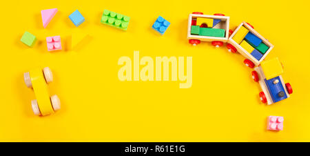 Baby kids toys background. Wooden train, car, colorful bricks and blocks on yellow background Stock Photo