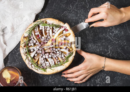 Woman's hands cut Apple pies with cranberry on black stone background. Top view. Stock Photo