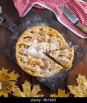 Baked whole round apple pie on a rectangular old brown board, wooden table, top view Stock Photo