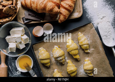 flat lay with dough for croissants on tray, yolk with brush and ingredients on table covered by flour Stock Photo