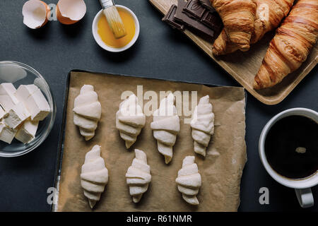 elevated view of tray with dough for croissants, ingredients and coffee cup on black table Stock Photo