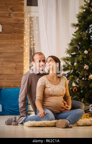 Photo of cheerful pregnant couple on background of decorated New Year tree,Cristmas interior Stock Photo