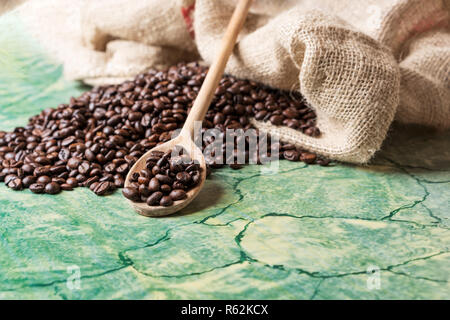 Coffee beans in coffee burlap bag on green surface and wooden spoon with coffee beans on top. Stock Photo