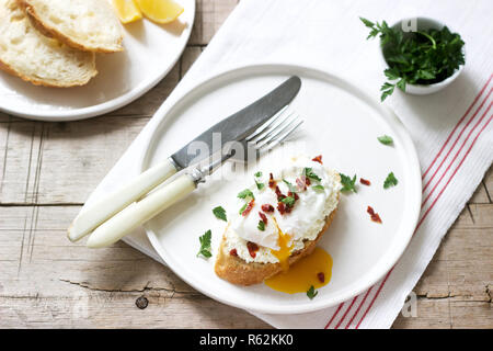 Crispy baguette toasts with cottage cheese, poached egg and dried tomatoes on a light background. Stock Photo