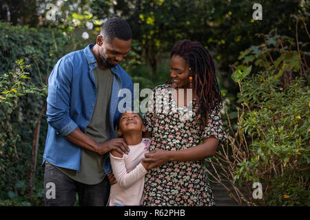A mother, father and daughter looking at each other lovingly in a park Stock Photo