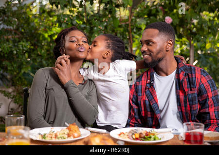 A family eating together, daughter kissing mother on the cheek Stock Photo