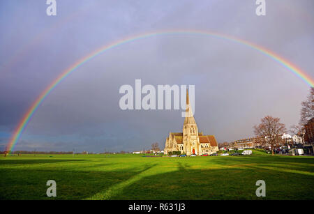 London, UK. 3rd December 2018. Seasonal weather - A rainbow appears over All Saints' Church in Blackheath in London as the sun breaks through the rainclouds. Stock Photo