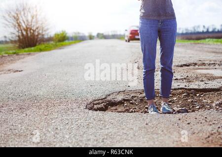 bad roads - a girl stands in a hole in the road Stock Photo