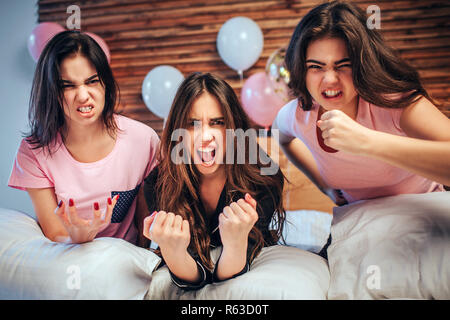 Emotional young women look on camera. They sit on bed with angry faces. Girls are very emotional Stock Photo