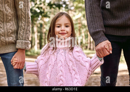 Close-up photo of cute little girl is holding parents hands during family walk