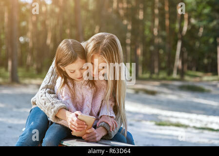 Mother holds laughing daughter and show her smart phone Stock Photo