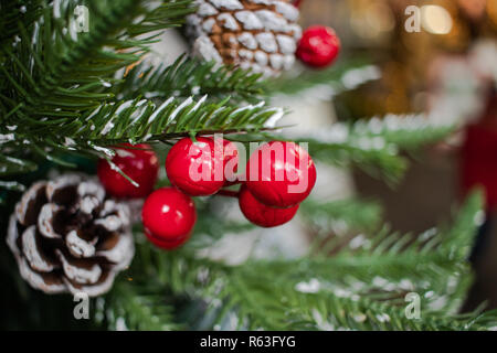 snowy pine cones hanging from a Christmas tree with red berries and Christmas lights Stock Photo