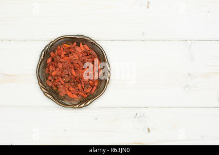 Lot of whole dried red goji berries in old iron bowl flatlay on white wood Stock Photo