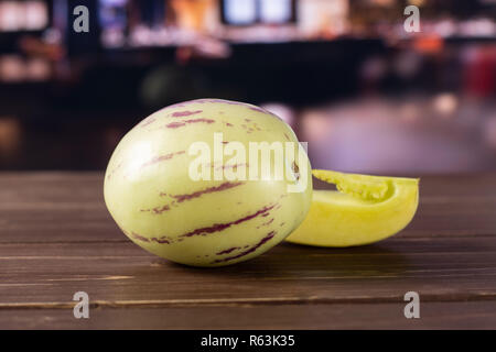 Group of one whole one slice of fresh striped pepino melon with restaurant in background Stock Photo