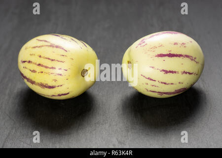 Group of two whole fresh striped pepino melon on grey stone Stock Photo