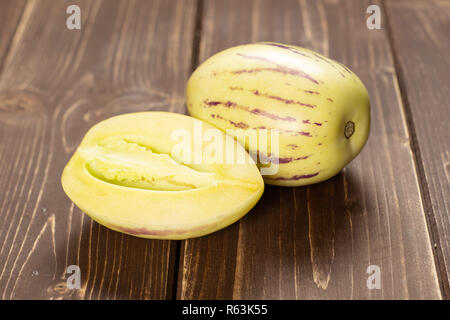 Group of one whole one half of fresh striped pepino melon on brown wood Stock Photo