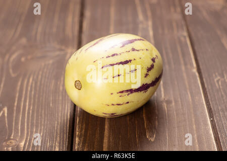 One whole fresh striped pepino melon on brown wood Stock Photo