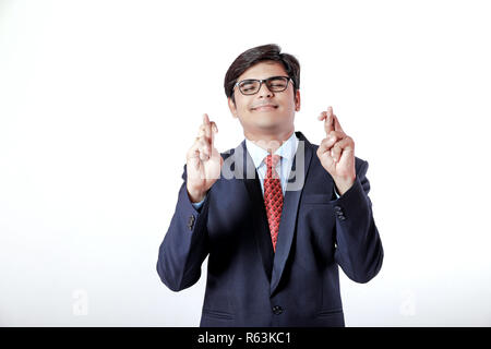 Young Indian businessman with his fingers crossing over white background Stock Photo