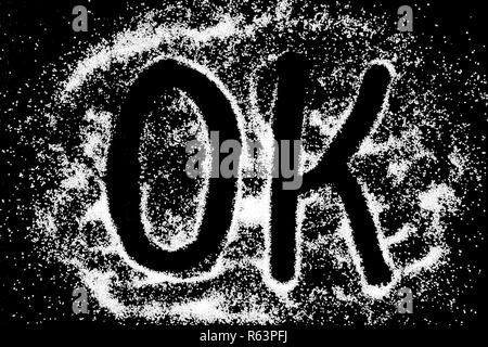 OK word symbol drawing by finger on white snow salt powder on black background. Capital letters Stock Photo