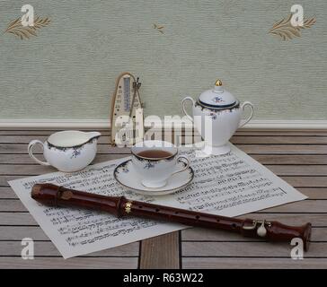 English teacup with saucer, cream jug and sugar bowl, fine bone china porcelain, metronome for music and a block flute on a sheet of music Stock Photo