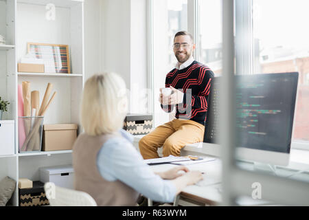 Cheerful office man drinking coffee while talking to coder Stock Photo