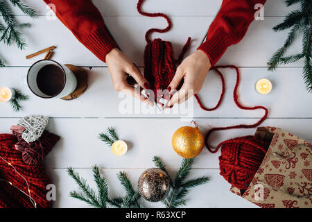Woman knits Christmas things on white wooden background. Stock Photo