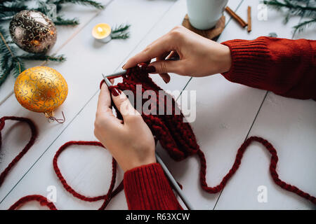 Woman knits Christmas things on white wooden background. Stock Photo