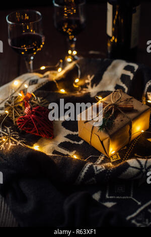 Christmas present with knitted sweater, Christmas lights and two glasses of wine. Stock Photo