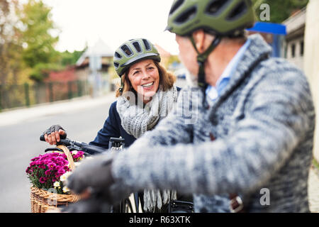Active senior couple with electrobikes standing outdoors on a road in town. Stock Photo