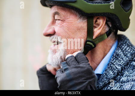 A close-up of active senior man standing outdoors, putting on bicycle helmet. Stock Photo