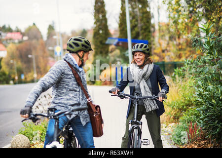 Active senior couple with electrobikes standing outdoors on pathway in town. Stock Photo