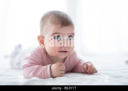 A portrait of baby girl lying on bed indoors. Stock Photo