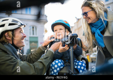 A small toddler boy with helmet and young parents outdoors in city. Stock Photo