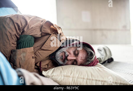 Homeless beggar man lying on the ground outdoors in city, sleeping. Stock Photo