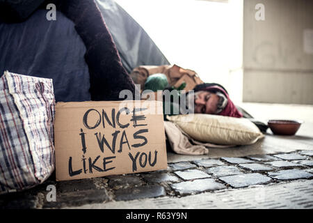 Homeless beggar man lying on the ground outdoors in city, sleeping. Stock Photo