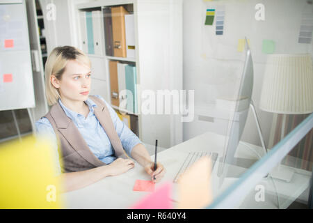 Pensive lady making notes while watching presentation in office Stock Photo