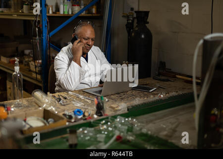 Worker talking on mobile phone while using laptop Stock Photo
