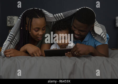Family using  mobile under the bed sheet while lying on bed Stock Photo