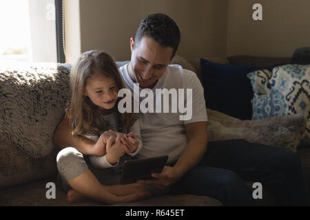 Father and daughter using digital tablet on sofa in living room Stock Photo