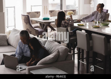 Grandfather and granddaughter using laptop on sofa in living room Stock Photo