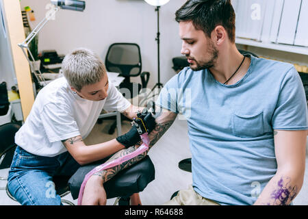 Blond short-haired tattoo artist working with remarkable tattoo Stock Photo