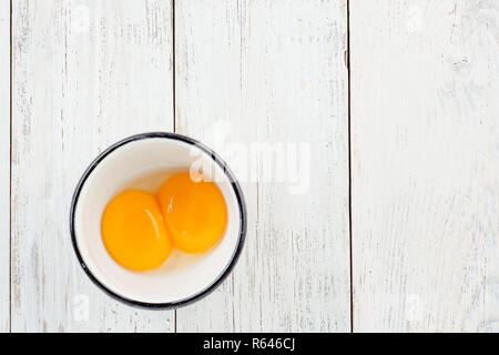 Bright yellow egg yolks in a white cup on wooden background with a blank space for a text, home kitchen decor concept, front view Stock Photo