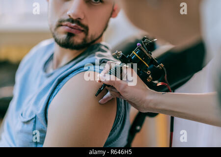 Attentive tattoo artist gently touching skin of her client with tattoo machine Stock Photo