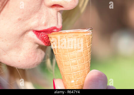 Young woman eating an Ice cream on warm summer day.Close up shot with ice cream touching red lips.Fragment of face and blurred background. Stock Photo